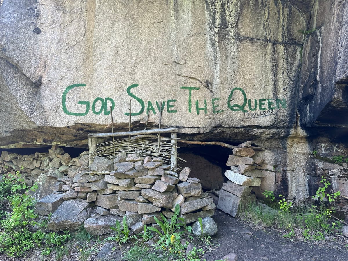 Trollbo — steinmuren og inngangen under berget, med «God save the Queen» malt over